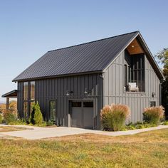 a large gray barn with a black roof and two garage doors on the side of it