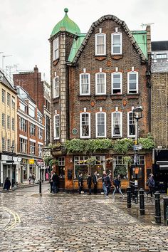 people are walking around in front of some buildings on a cobblestone street with green roofs