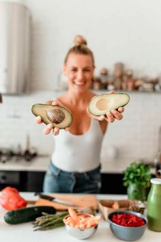 a woman holding an avocado in one hand and some carrots on the other