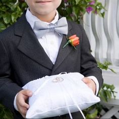 a young boy in a tuxedo holding a white bag with two roses on it