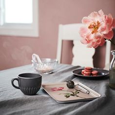 a table topped with plates and cups next to a vase filled with pink flowers on top of a wooden table