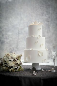 a white wedding cake sitting on top of a table next to a wine glass and flower bouquet