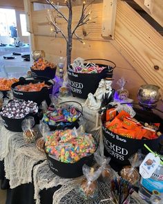 a table topped with black buckets filled with candy next to a tree and halloween decorations