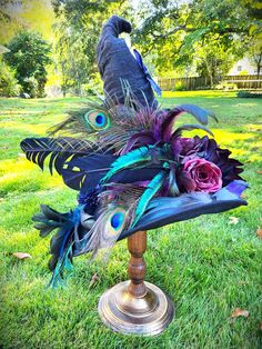 a hat with peacock feathers and flowers on it in the middle of a grassy field