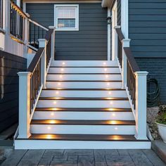 some lights are lit up on the steps in front of a house that is painted black and white