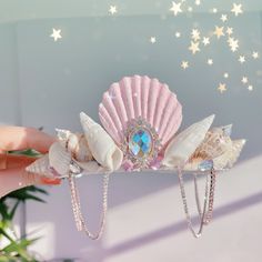 a hand holding a pink and white hair comb with shells on it's side