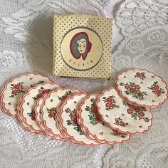 a set of six plates sitting on top of a white lace tablecloth next to a box