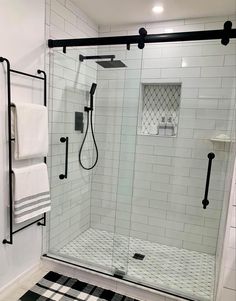 a bathroom with black and white checkered rugs on the floor, glass shower door, and towel rack