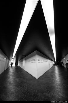 a black and white photo of people walking in an empty room with lights on the ceiling