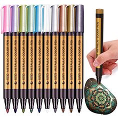 a hand holding a pen with eight different colored pens in front of it and an image of