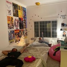 two people laying on beds in a bedroom with posters on the wall and windows above them