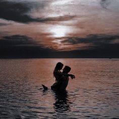 two people in the water at sunset, one is holding the other's head