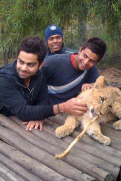 three men pose with a lion cub on a wooden platform in front of some trees