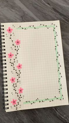 an open notebook with pink flowers and vines on the cover, sitting on a marble surface