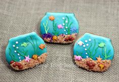 three decorated cookies sitting on top of a cloth covered table next to an ocean scene