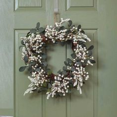 a wreath hanging on the front door with white flowers and greenery around it's edges