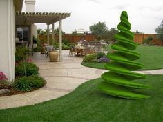 a green sculpture in the middle of a yard next to a patio and table with chairs