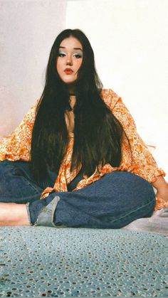 a woman sitting on the floor with her legs crossed and eyes closed, wearing blue jeans