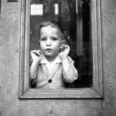 a little boy standing in front of a window with his hands up to his face