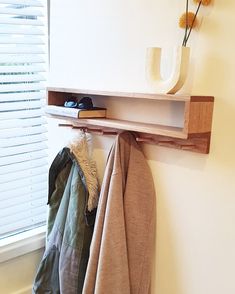 a coat rack with clothes hanging on it next to a window and a flower in a vase