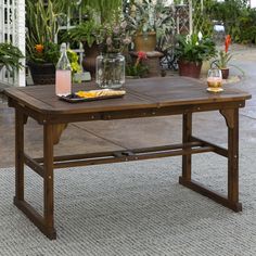 a wooden table sitting on top of a rug next to potted plants and flowers