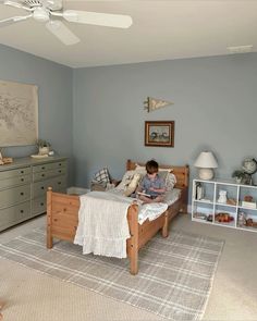 a young boy sitting on his bed reading a book in the corner of this bedroom