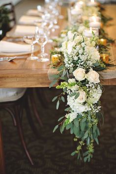 a long table with white flowers and greenery is set up for a formal dinner