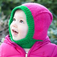 a small child wearing a pink jacket and green knitted hat looking up to the sky