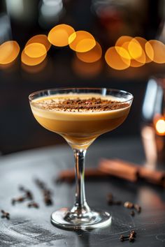 a drink in a glass on a table next to some coffee beans and cinnamons