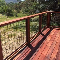 a wooden deck with metal railings and wire fencing on it, overlooking a wooded area