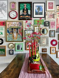 a wooden table topped with a vase filled with flowers next to a wall covered in pictures