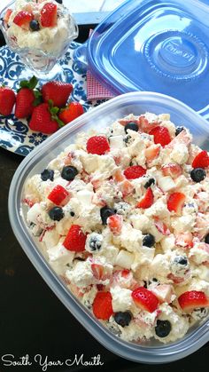 a plastic container filled with fruit salad next to a bowl of strawberries and blueberries