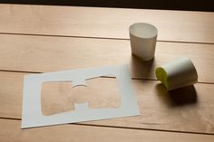 a cut out piece of paper sitting on top of a wooden table next to a cup