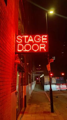 a red neon sign that reads stage door on the side of a building at night