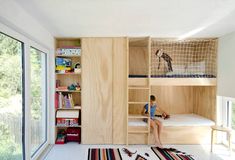 a child sitting on the bottom bunk of a bunk bed in a room with windows