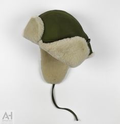 A classical and a very practical aviator hat can now accompany you in a daily basis . Proposed for men and women of every age. Very comfortable and easy to wear . An Aviator Napa Sheepskin hat with earflaps and leather strings . It has three little links-holes to let the sound pass through . This great everyday hat is made of olive green napa sheepskin , the outer part , and soft white merinos sheepskin wool the inner and front part . It is very light and extremely durable to any conditions. It Winter Military Hat With Curved Brim, Adjustable Winter Hunting Hat, Winter Hunting Hats With Adjustable Fit, Adjustable Windproof Aviator Hat, Adjustable Windproof Hat With Ear Flaps, Adjustable Faux Fur Lined Hat With Ear Flaps, Vintage Hats With Adjustable Ear Flaps, Sheepskin Hats With Ear Flaps For Outdoor, Vintage Adjustable Winter Bonnet