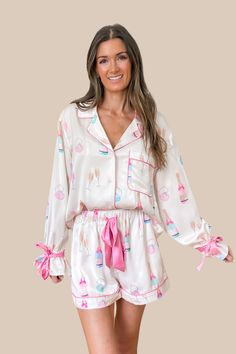 Perfect for Brides, Bachelorette parties, getting ready on your wedding day, honeymoons, or the best gift for brides at showers and bachelorette parties! Our Champagne Ribbon Bow Satin Pajamas Set in Ivory and Pink features a collared neckline, button up top with ivory satin fabric featuring prints of champagne bottles and rings on cushions throughout, chest pocket, long sleeves, and pink ribbon ties around ruffled cuffs. Shorts feature an elastic waist with pink ribbon bow tie closure for adjus Best Gift For Bride, Bride Pajama, Bridal Party Pajamas, Olive Clothing, Style Steal, Satin Pyjama Set, Satin Pajamas, Jumpsuit Shorts Rompers, Sweater Blouse