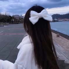 a woman with long hair and a bow in her hair is looking at the water