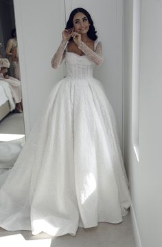 a woman standing in front of a mirror wearing a white wedding dress with long sleeves