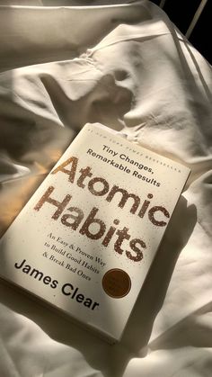 the book atomic habitts is laying on top of a bed with white linens