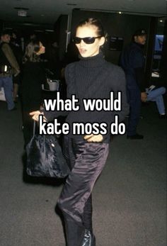 a woman in black sweater and pants walking through an airport with her hand on her hip