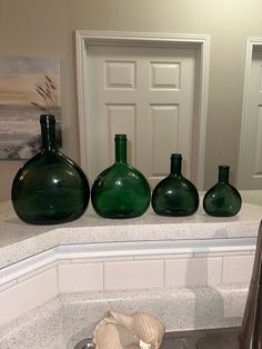 three green glass vases sitting on top of a counter next to a white door