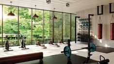 there is a gym with many exercise equipment in the room, and it has large windows that look out onto the trees