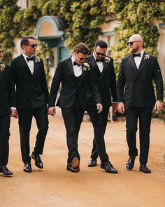 a group of men in tuxedos walking down a dirt road