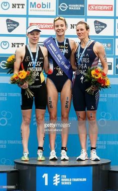 three women standing on top of a podium with medals in their hands and wearing swimsuits