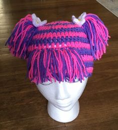 a knitted hat with pink and purple fringes on top of a mannequin head