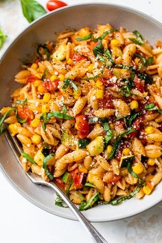 a bowl filled with pasta and vegetables on top of a white table next to a fork