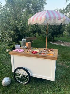 an ice cream cart is set up in the grass with a pink and white umbrella