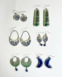 nine pairs of earrings are displayed on a white surface, each with different designs and shapes