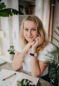 a woman sitting at a desk with her hand on her chin and looking into the camera